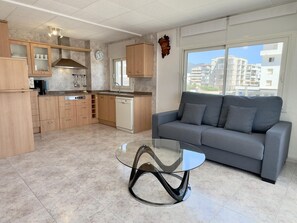 Eine moderne Küche mit Holzsäcken, einem Geschirrspüler und einem Essbereich mit Glastisch und grauem Sofa.