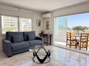 Ein modernes Wohnzimmer mit grauem Sofa, einem Glastisch und einem Essbereich mit Holzstühlen.
