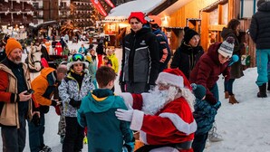 A snowy outdoor scene with people, including a person dressed as Santa Claus, in a town square with buildings and a sign that reads "SKISEX".
