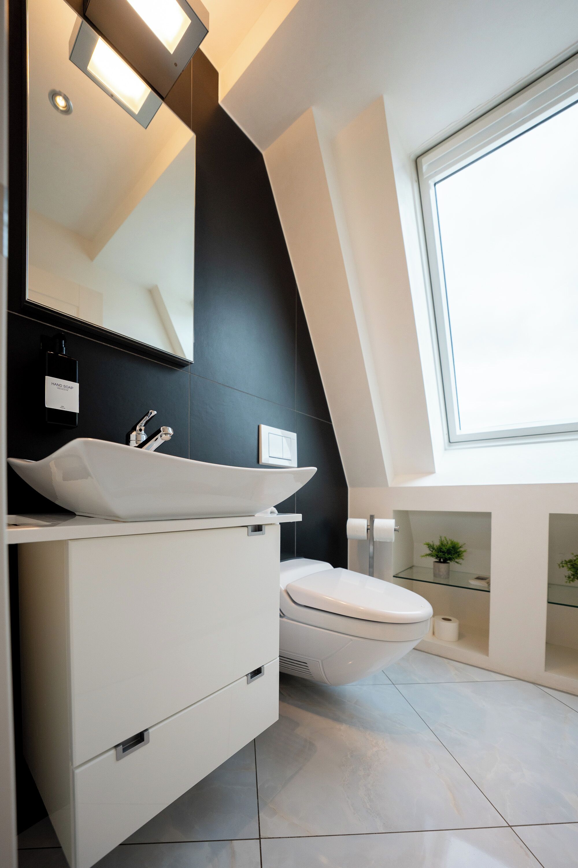 Un bagno moderno con lavandino bianco, un water, uno specchio grande e un lucernario.