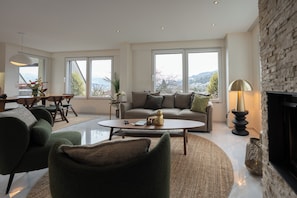 Un salon moderne avec un canapé, une table basse et des fauteuils, de grandes fenêtres offrant une belle vue et une cheminée.