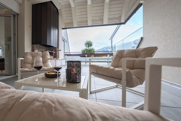 Un espace extérieur moderne, aménagé avec une table en verre, deux fauteuils confortables et une bougie décorative.