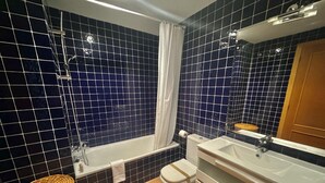 A bathroom with dark blue tiled walls, a white bathtub, a white toilet, and a white sink with a mirror above it. - Apartment with terrace near the beach in Roses (Roses)