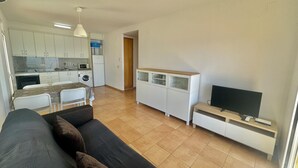 A compact living space with a sofa, a TV, a kitchen area with appliances, and a dining table. - Apartment with terrace near the beach in Roses (Roses)