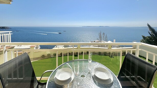 A balcony with a glass table and chairs, overlooking a clear blue sea and a distant coastline. - Apartment with terrace near the beach in Roses (Roses)