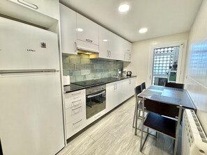 Une cuisine moderne avec des armoires blanches, un comptoir noir et un four encastré. On y trouve également un coin repas avec une table et des chaises.