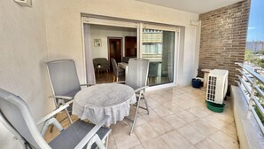 Ein Balkon mit Tisch und Stühlen, eine Schiebeglastür, die zu einem Essbereich führt, und eine Backsteinmauer.
