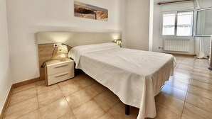 Ein Schlafzimmer mit einem Bett, Nachttischen, einem Wandbild und einem Fenster mit Jalousien.