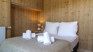 A wooden-paneled room with a bed, white linens, a bedside lamp, and rolled towels on the bed. - Ski-in/ski-out apartment for families with balcony and parking (Courchevel 1650)