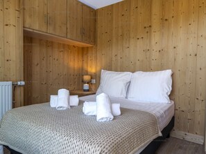 Ein Zimmer mit Holzwänden, ausgestattet mit einem Bett, weißen Leinentüchern, einer Nachttischlampe und aufgerollten Handtüchern auf dem Bett.