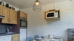A compact kitchen with wooden cabinets, a built-in microwave, a dishwasher, and a dining area with a table set for two. - Ski-in/ski-out apartment for families with balcony and parking (Courchevel 1650)