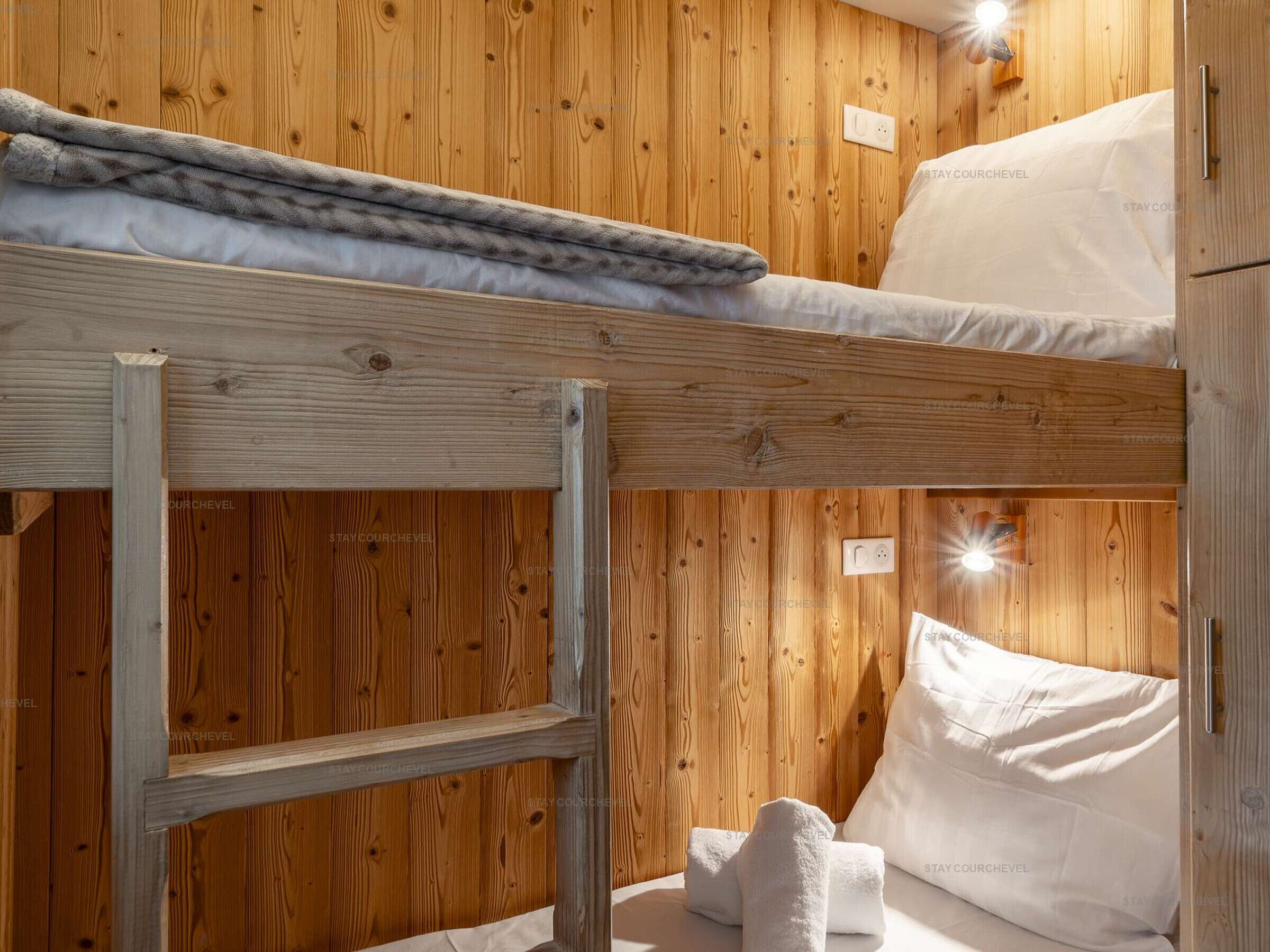 Un lit superposé avec une échelle, des murs en bois et une table de chevet avec une lampe.
