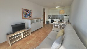 A modern living room with a flat-screen TV, a sofa, and a dining area with a table and chairs. - Beautiful apartment with pool, WiFi and parking, 10 min from the beach (Roses)