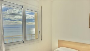 A room with a bed and a window overlooking a balcony with a view of the sea. - Beautiful apartment with pool, WiFi and parking, 10 min from the beach (Roses)