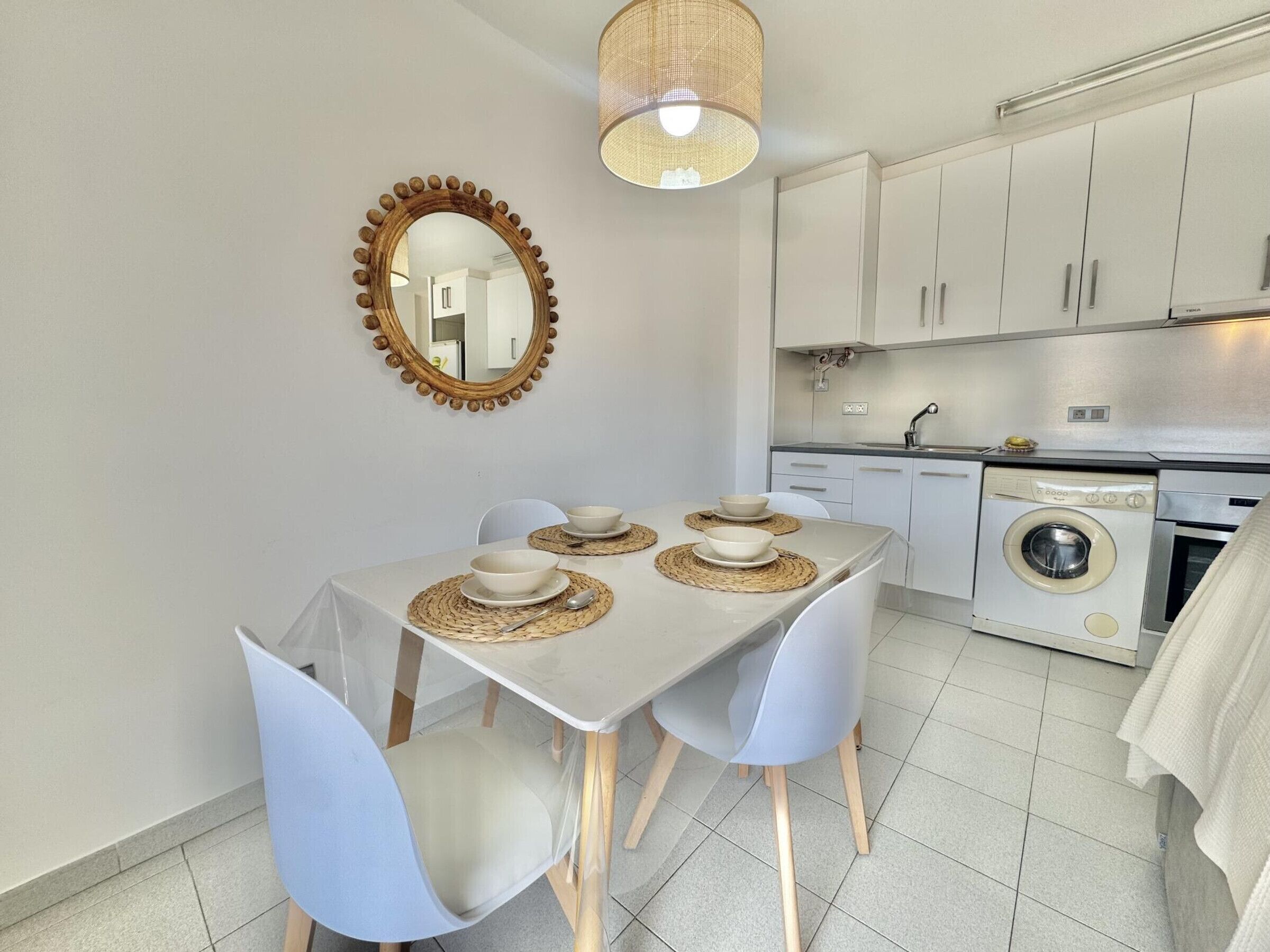A modern kitchen with white cabinets, a washing machine, and a dining area with a table set for four.