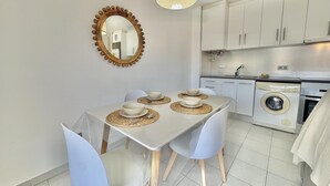 Una cocina moderna con armarios blancos, lavadora y comedor con mesa para cuatro.