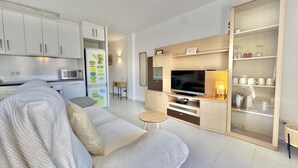 Una sala de estar moderna con sofá, televisión y una zona de cocina con armarios y microondas.
