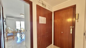 A hallway with a wooden door, a notice on the door, and a dining area in the background. - Charming Apartment in Central Roses, 400m from Beach with Private Parking and Wi-Fi (Roses)