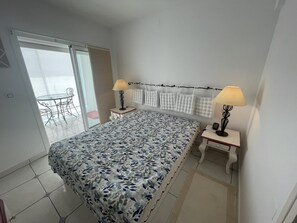 A bedroom with a bed, two bedside tables with lamps, a window with curtains, and a balcony with a table and chairs. - Beautiful 3-bedroom apartment with AC, parking, and Wifi in Roses (Roses)
