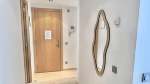 A hallway with a wooden door, a wall-mounted mirror, and a light switch. - Spacious Apartment in Central Roses, 650m from Beach, with Terrace & Private Parking (Roses)