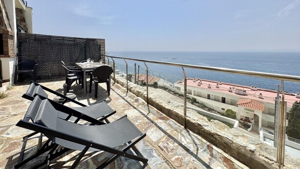 Una terraza con mesa y sillas, un área de piscina con sillones de descanso y vista al mar.