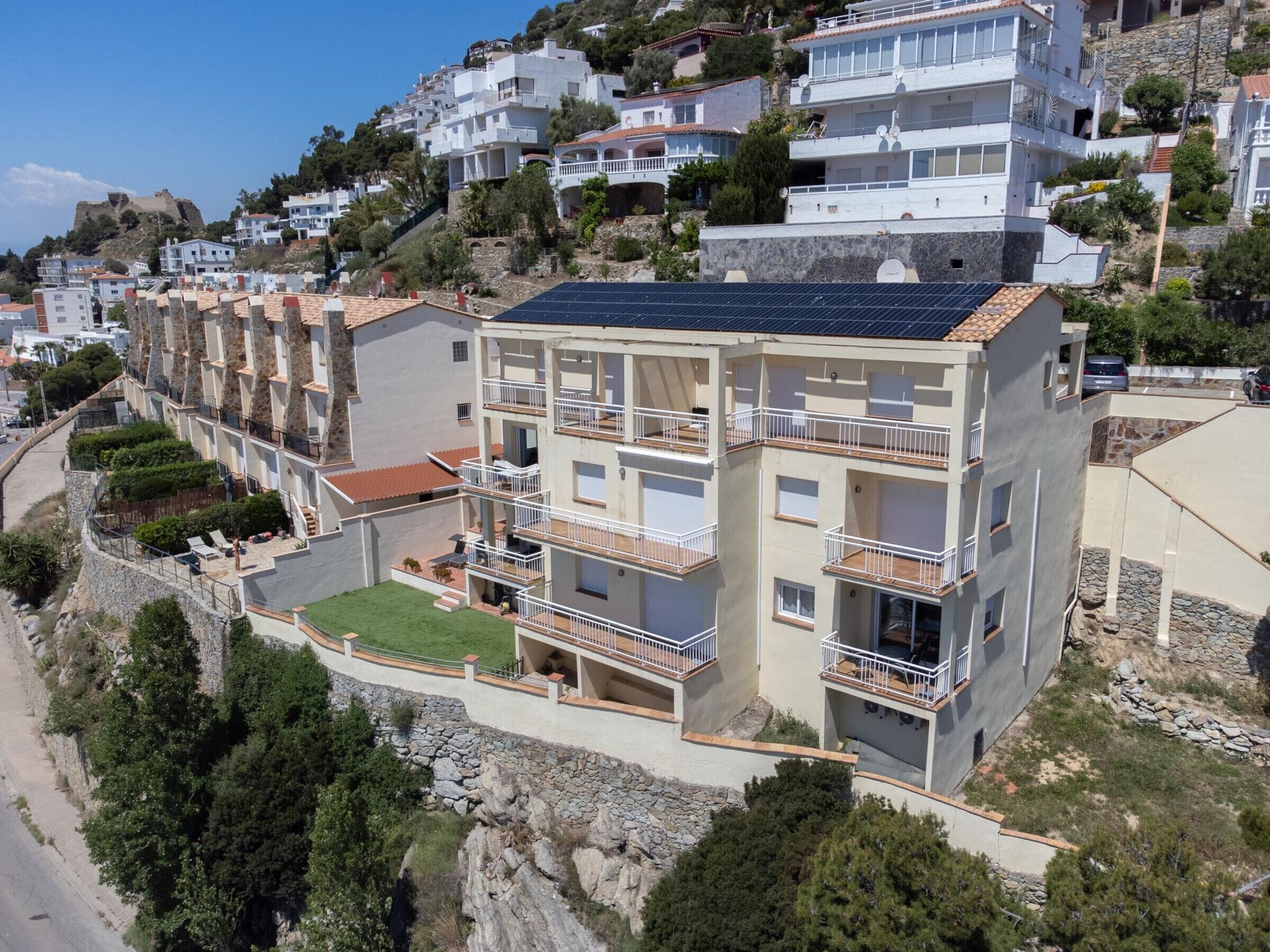 A multi-story residential building with balconies, a rooftop solar panel, and a surrounding landscaped area.
