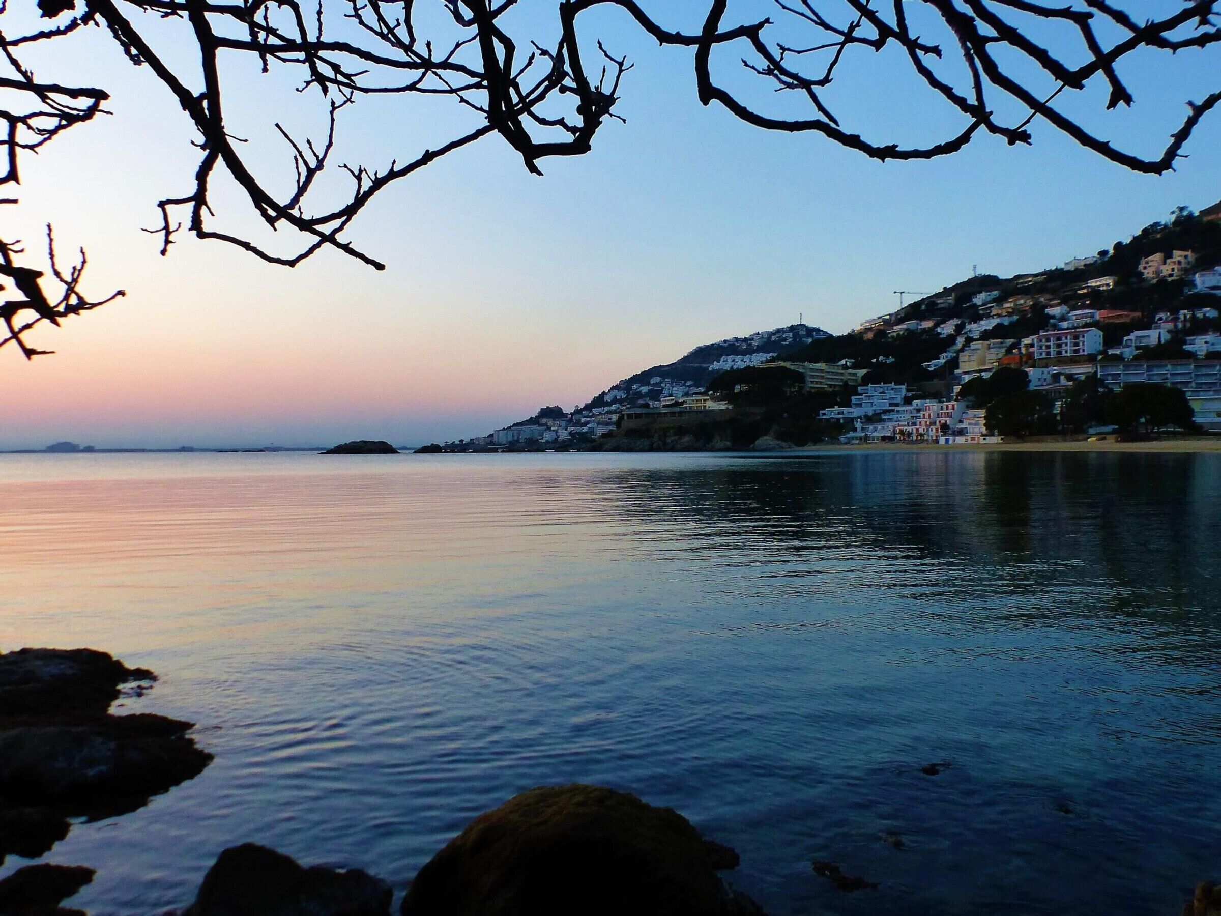 A coastal town with buildings on a hillside overlooking calm waters.