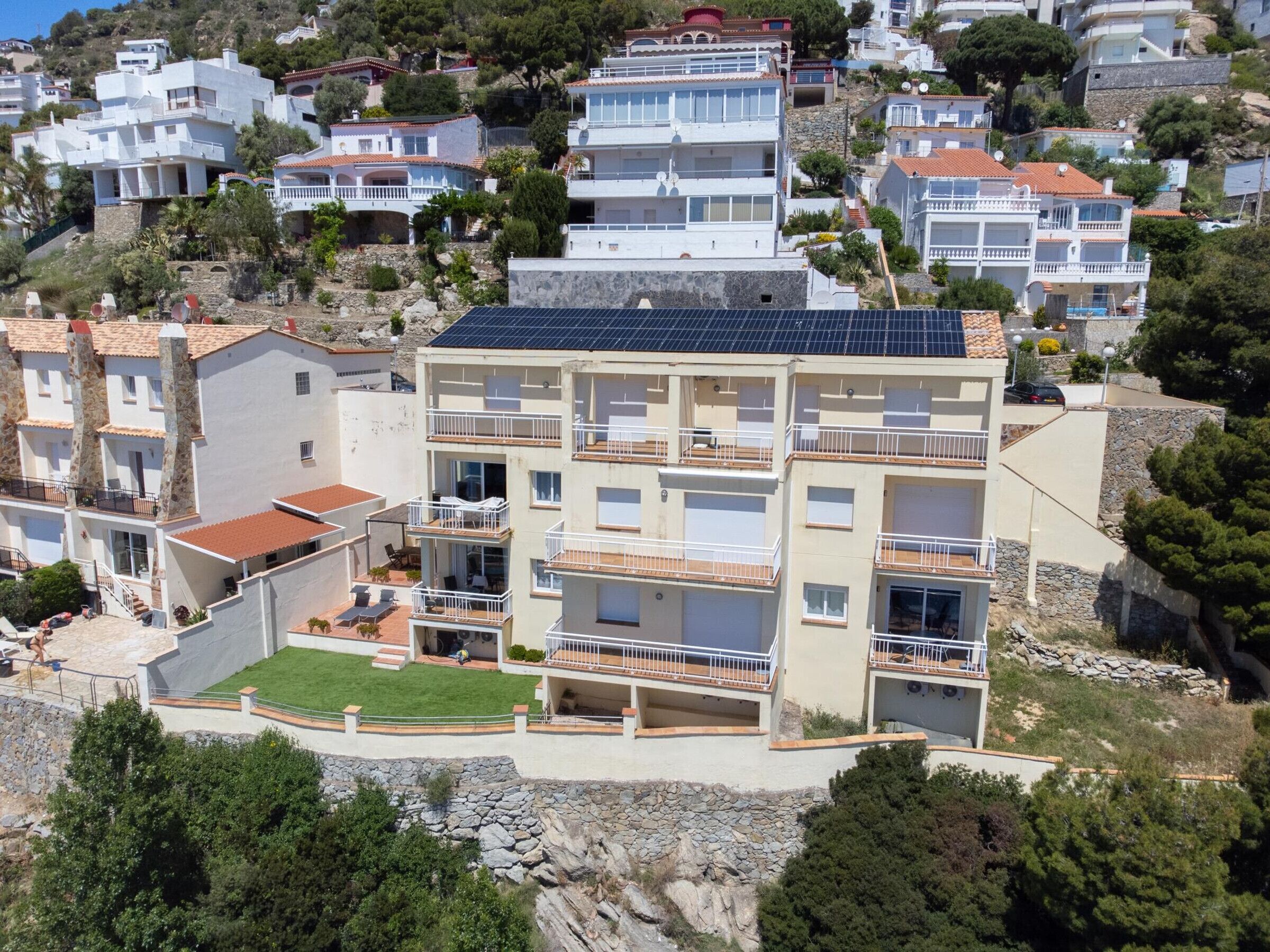 A multi-story residential building with balconies, a rooftop solar panel, and a small garden area.