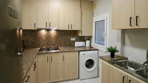 Een kleine keuken met een gasfornuis, een ingebouwde wasmachine en een raam met een matglazen deur.