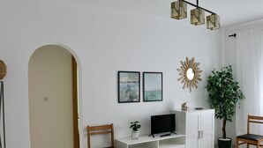 Een moderne woonkamer met een witte kast, twee ingelijste kunstwerken, een televisie en een potplant.
