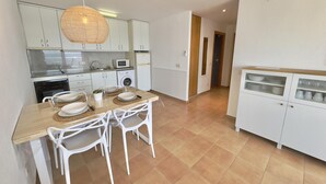 A modern kitchen with white cabinets, a dining table with chairs, a microwave, and a washing machine. - Beautiful apartment with pool, air conditioning, and parking 700m from Roses beach (Roses)