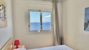 A bedroom with a bed, a window with a view of the sea, a red lamp, and a painting on the wall. - Beautiful apartment with pool, air conditioning, and parking 700m from Roses beach (Roses)