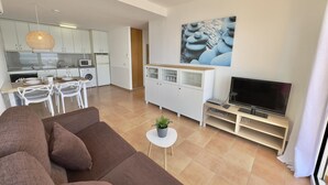 A modern apartment with a living room, dining area, and kitchen. There is a flat-screen TV, a dining table with chairs, a sofa, and a cabinet with glass doors. - Beautiful apartment with pool, air conditioning, and parking 700m from Roses beach (Roses)