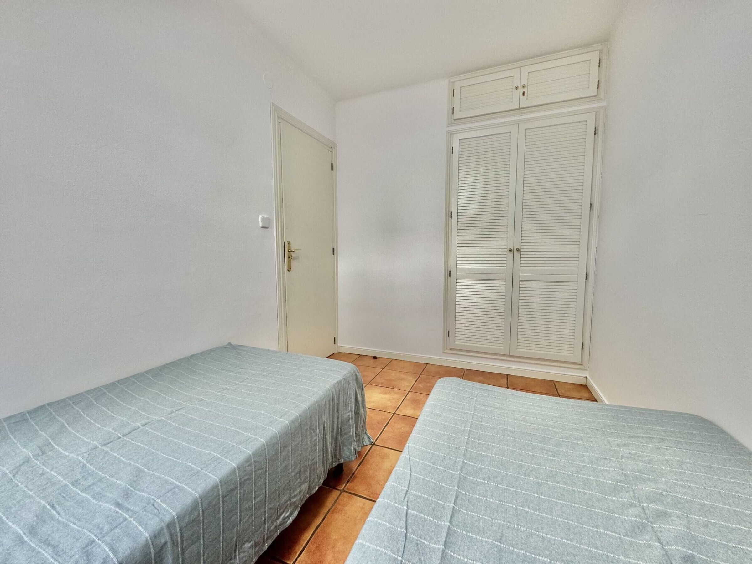A small room with two single beds, a white door, and a white wardrobe with louvered doors.