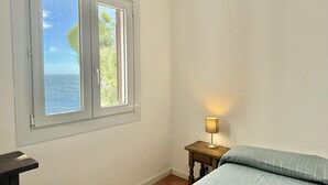 Une chambre à coucher avec un lit, une table de chevet avec une lampe, une fenêtre donnant sur la mer et une porte.