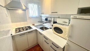 Une cuisine de taille réduite avec des meubles blancs, une cuisinière à gaz, un évier, un grille-pain et un réfrigérateur.