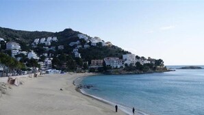 Una playa con una orilla arenosa, algunas personas y edificios en una colina al fondo.