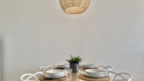 Una mesa de comedor con sillas blancas, una lámpara colgante de fibra y una planta en maceta.