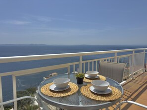 A round glass table with woven placemats, two white bowls, and a small potted plant on a balcony overlooking the sea. - Beautiful apartment with pool, WiFi, AC and parking 700m from beach (Roses)