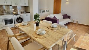 A modern kitchen with white cabinets, a washing machine, and a dining area with a wooden table and chairs. - Apartment with pool, AC, and parking 700m from the beach in Roses (Roses)