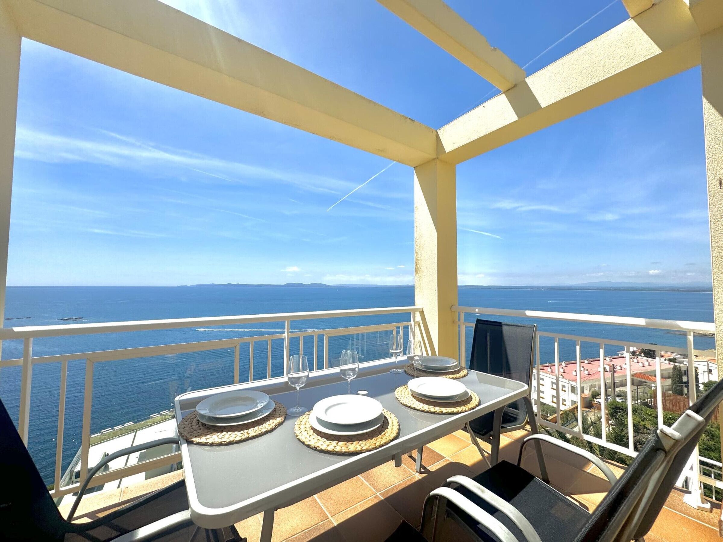 A balcony with a table set for dining, overlooking a coastal view.