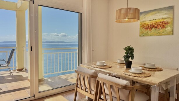A dining area with a view of the sea, a wooden table, chairs, a hanging light, and a painting on the wall. - Apartment with pool, AC, and parking 700m from the beach in Roses (Roses)