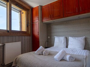 A bedroom with a wooden headboard, a large window, and a bed with white linens and towels. - Comfortable apartment for 6 in Courchevel, direct ski-in/ski-out (Courchevel 1650)