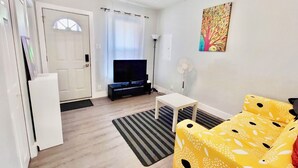 A living room with a TV, a sofa, a small table, and a fan. - Mid-term stay 3BR Furnished House(monthly rental) (Hamilton)