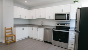 A modern kitchen with white cabinets, stainless steel appliances, and a wooden chair. - Mid-term stay 3BR Furnished House(monthly rental) (Hamilton)