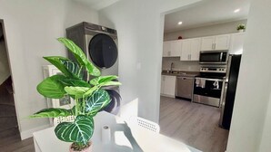 A modern kitchen with white cabinets, stainless steel appliances, and a dining area with a white table and a potted plant. - Mid-term stay 3BR Furnished House(monthly rental) (Hamilton)
