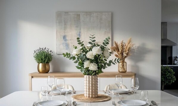 A dining table set with plates, glasses, and cutlery, a vase with white flowers, and two potted plants on a wooden console. - Caporizon-Villa Aubepines (Coulounieix-Chamiers)