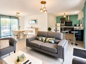A modern living room with a grey sofa, a dining area with a white table, and a kitchen with stainless steel appliances. - Caporizon-Villa Aubepines (Coulounieix-Chamiers)