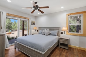 A bedroom with a bed, two bedside tables, a ceiling fan, and a window with a view of trees. - Lovely 2-bedroom cabin bordering Zion's national Park, Close to cable Mountain. (Orderville)