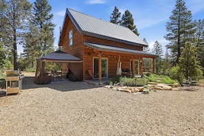 A wooden cabin with a covered patio, gravel ground, and surrounding trees. - Lovely 2-bedroom cabin bordering Zion's national Park, Close to cable Mountain. (Orderville)